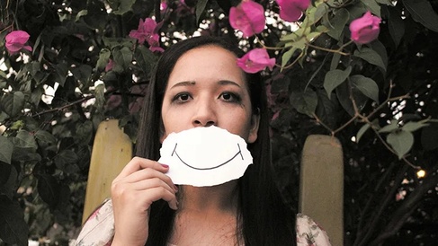 Sad Young woman, running eye make-up, holds a large white card with hand drawn smile over her mouth
